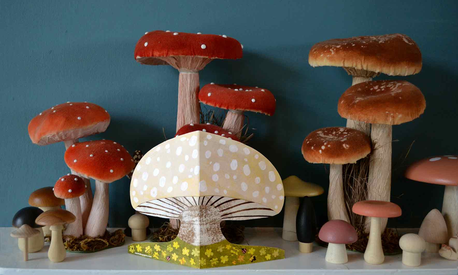 Mushroom shaped greeting card surrounded by an assortment of mushroom decor on a white shelf.