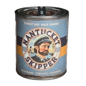 A cylindrical wax candle tin labeled "Buster Mandel Nantucket Skipper Mahogany, Tobacco & Cashmere Candle." The label art features a skipper in a maritime scene, highlighting our small batch candle infused with essential oils.
