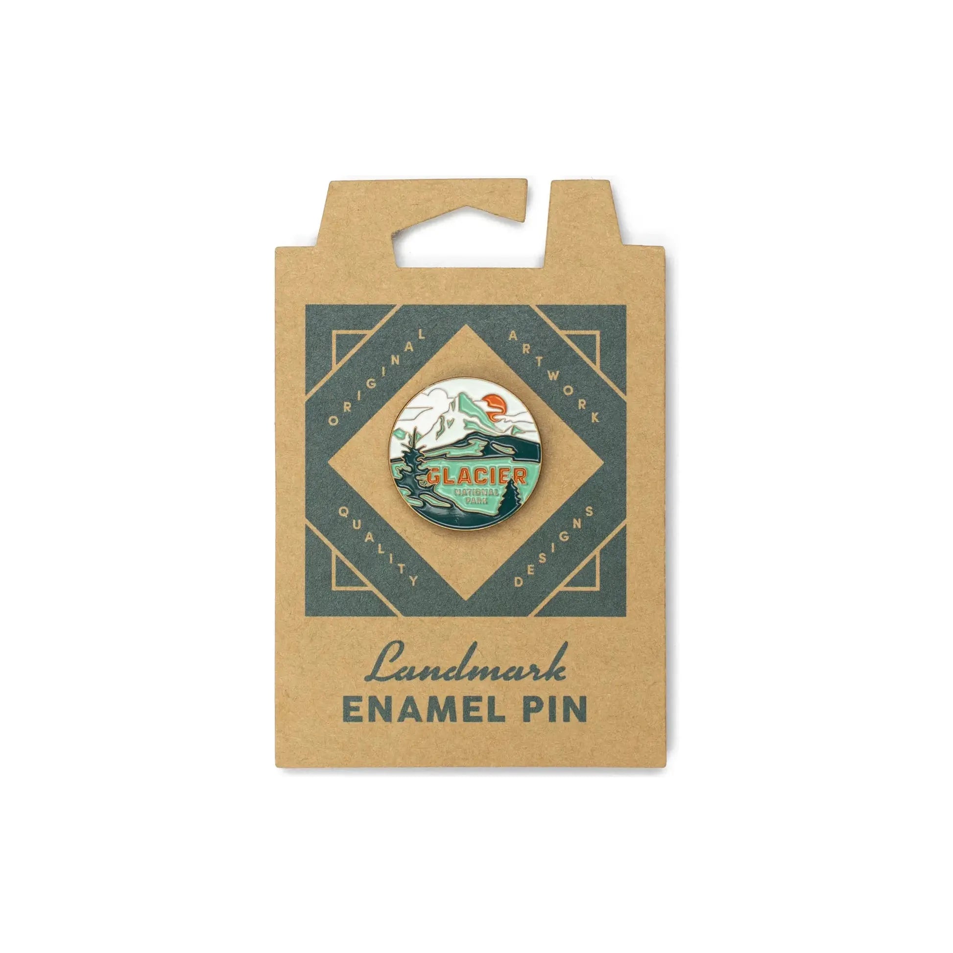 A round enamel pin featuring a glacier scene with mountains and text saying "GLACIER NATIONAL PARK" is attached to a brown cardboard backing made from sustainable packaging, sold under the name The Landmark Project Glacier National Park Pin.