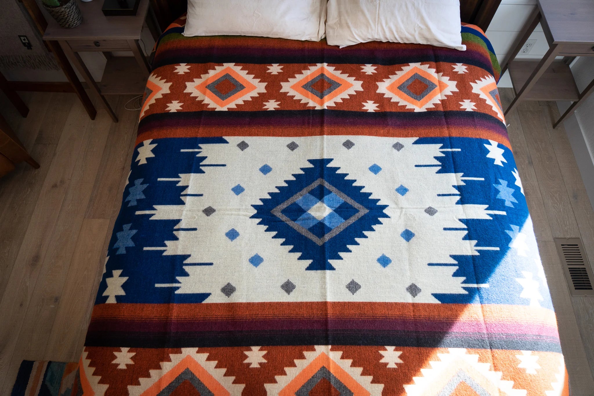 Top view of bed showcasing Alpaca Threadz Moab Orange Western Native Blanket in blue, orange, white, brown; artisan bedding.