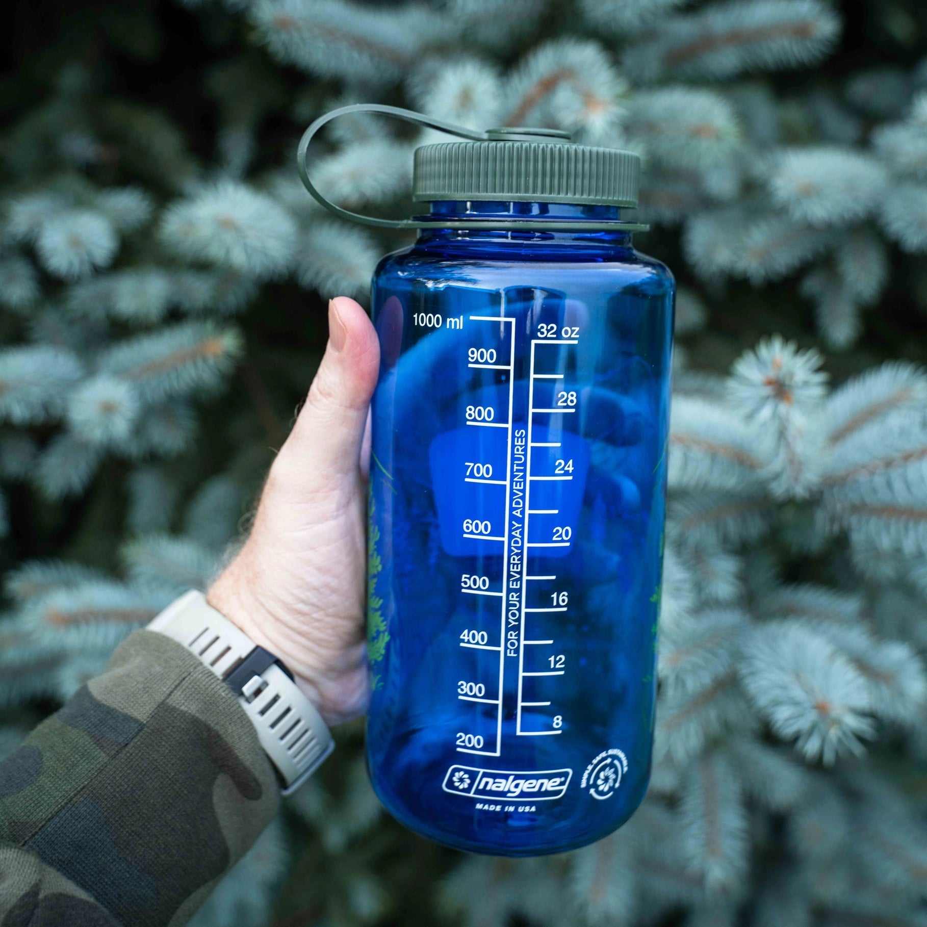 Forager Provisions LTD blue 32oz Nalgene water bottle with Snort Pines Not Lines graphic held against pine branches
