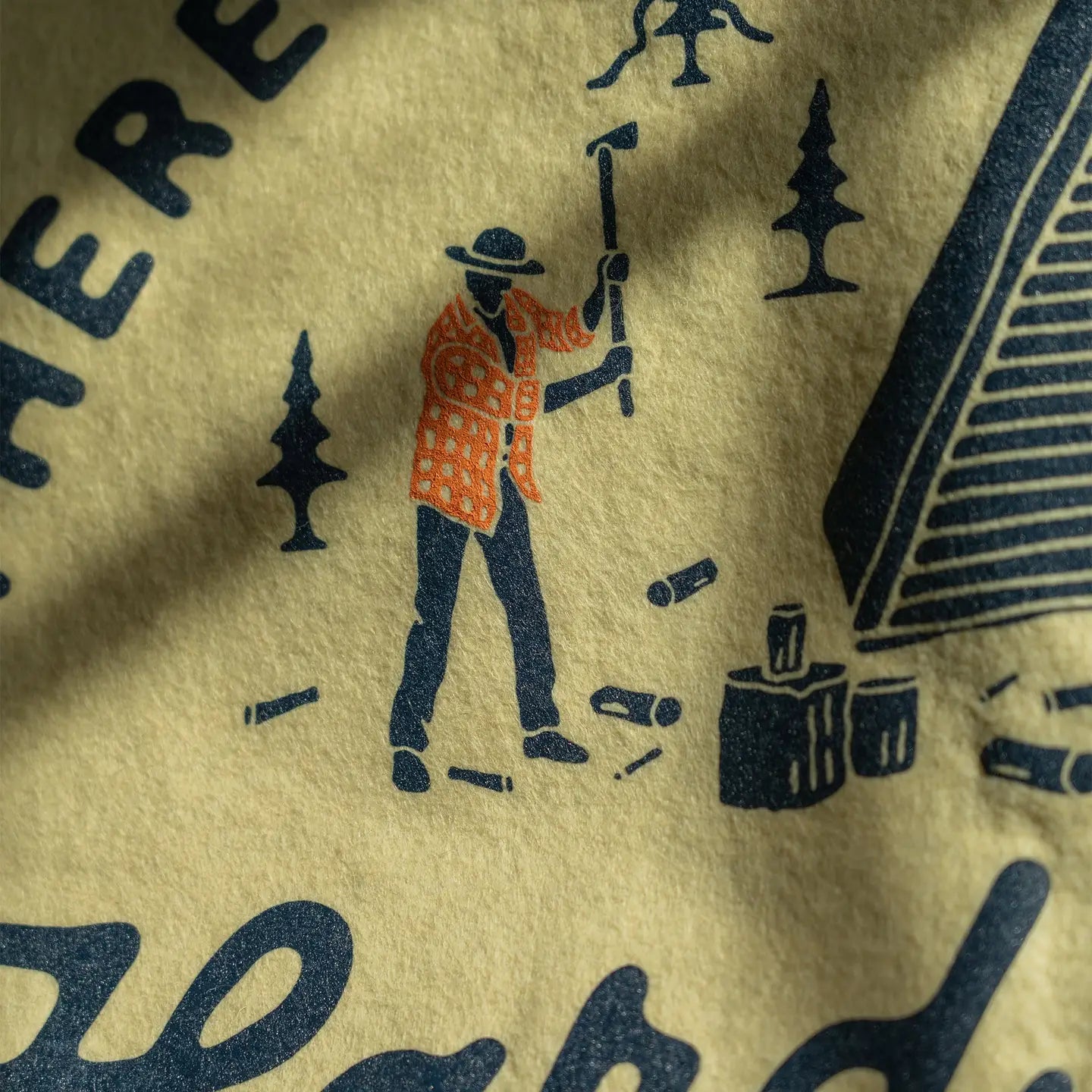 Person chopping wood by a cabin with Oxford Pennant "There Is No Substitute For Hard Work" flag, outdoors camping scene.
