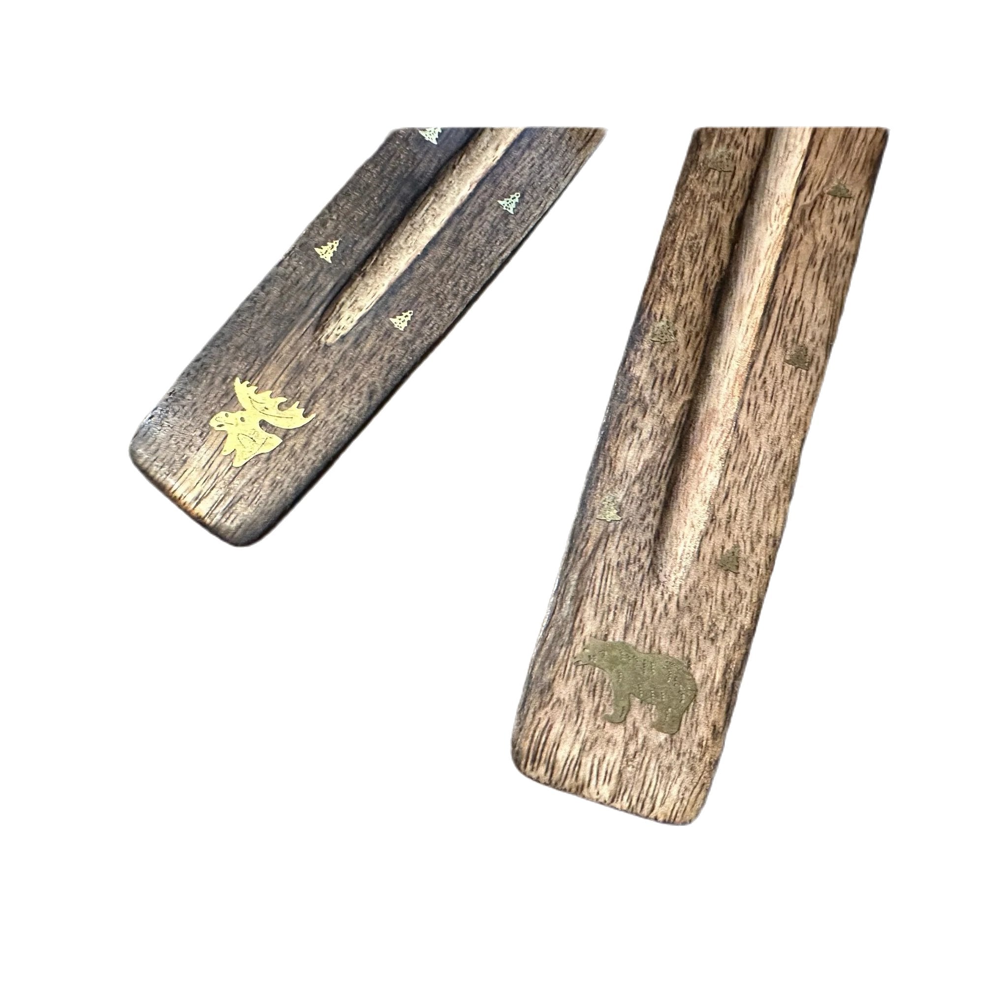 Two PAINES Wood Ash Catcher Incense Holders, one featuring a moose and the other a bear, rest on a rustic wooden surface.