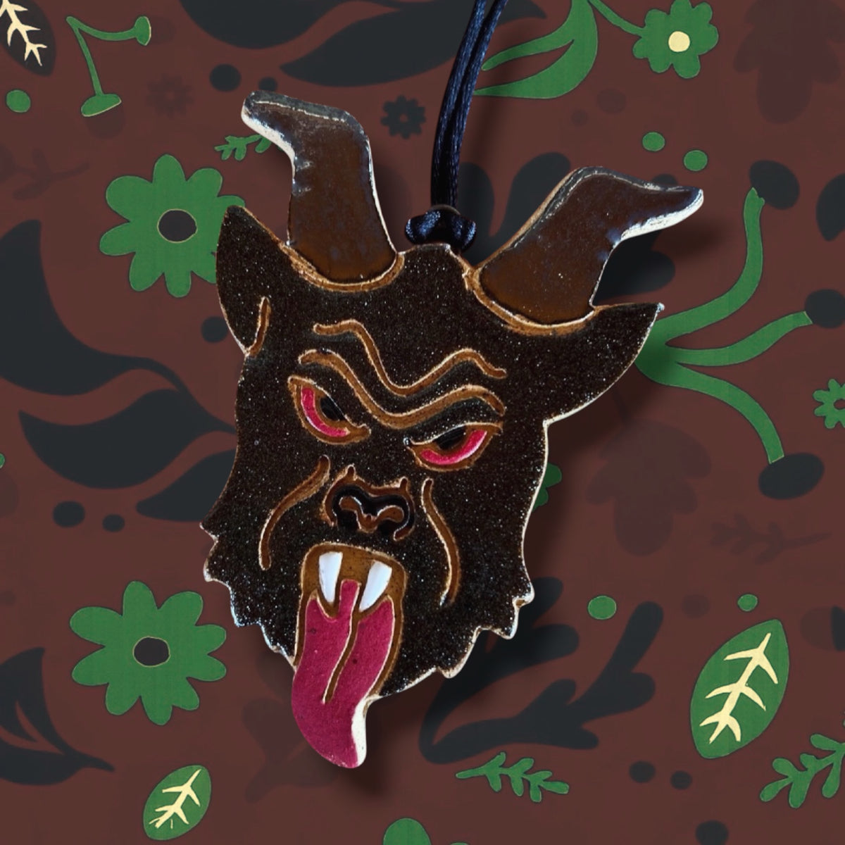 Handmade Tough Kitty Krampus Ornament—horned, red-eyed creature with floral backdrop. Limited edition, add to wishlist now!.