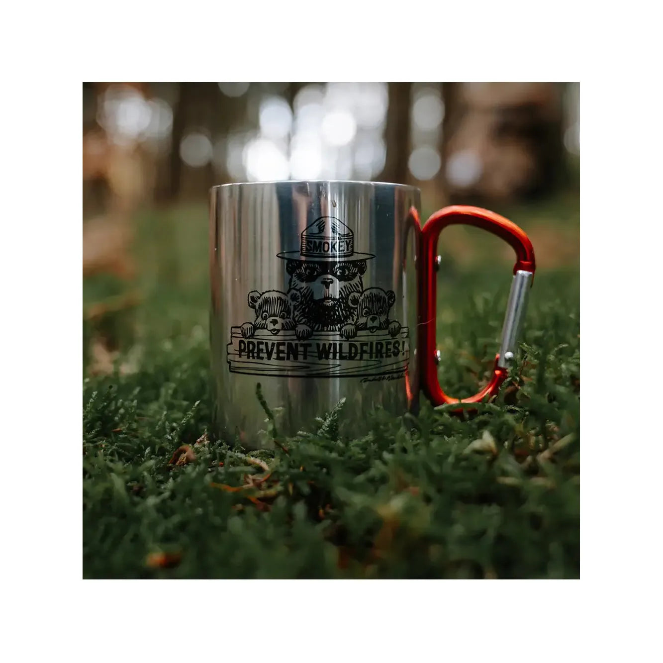 The Smokey Bear Carabiner Handle Mug - Smokey Friends, made of stainless steel and equipped with a red handle, showcases a cartoon of Smokey Bear with cubs, advocating "Prevent Wildfires!