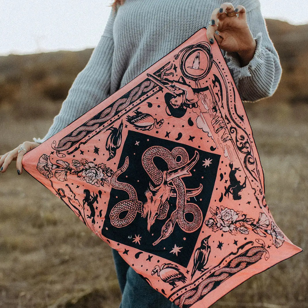 Person holding Rattle & Hiss Bandits Bandana, orange organic cotton square, outdoors. Eco-friendly bandana accessory.
