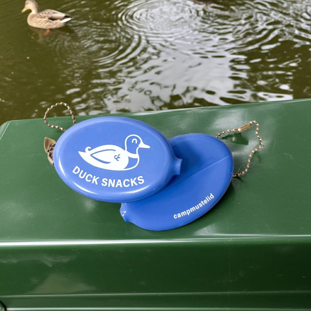 Forager Provisions LTD blue rubber snap-top coin wallet with Duck Snacks print resting on a green park bench
