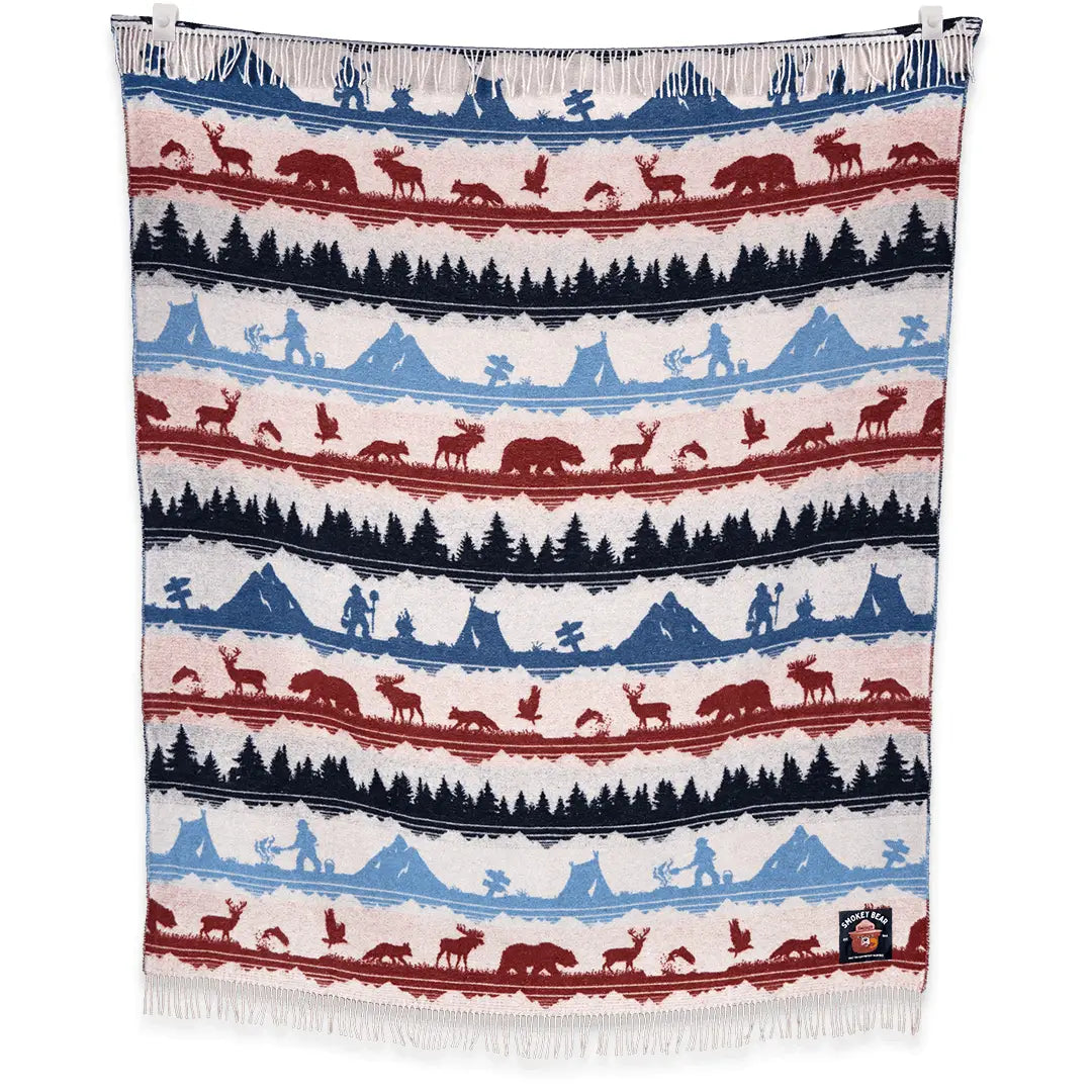 Introducing the Sackcloth & Ashes Smokey Bear Blanket - Smokey Ramble, adorned with alternating rows of red and blue forest and mountain patterns, featuring bears, deer, and other wildlife. This beautifully designed blanket is perfect for promoting wildfire prevention or as a thoughtful donation to a homeless shelter.