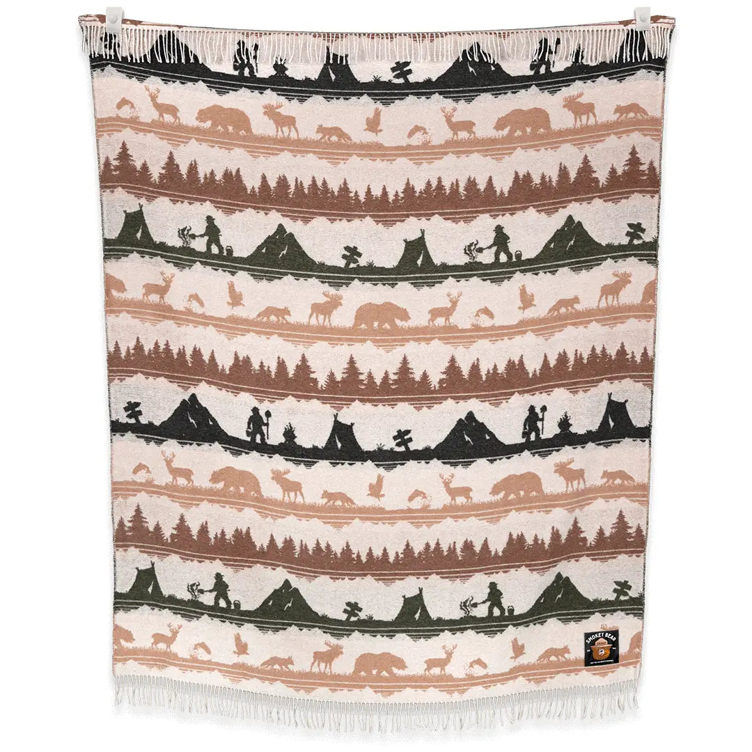The Sackcloth & Ashes Smokey Bear Blanket - Smokey Ranger features a stunning nature-themed design with silhouettes of trees, mountains, animals, and hikers in muted earth tones. This distinctive blanket not only supports wildfire prevention but is also made from recycled materials for an eco-friendly touch.