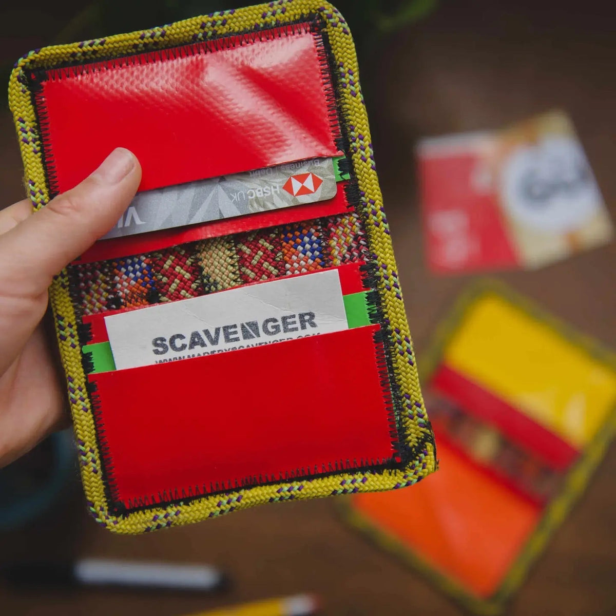 Hand holding Scavenger Upcycled Climbing Rope Wallet - Fire, red card slots shown with visible Scavenger loyalty card.