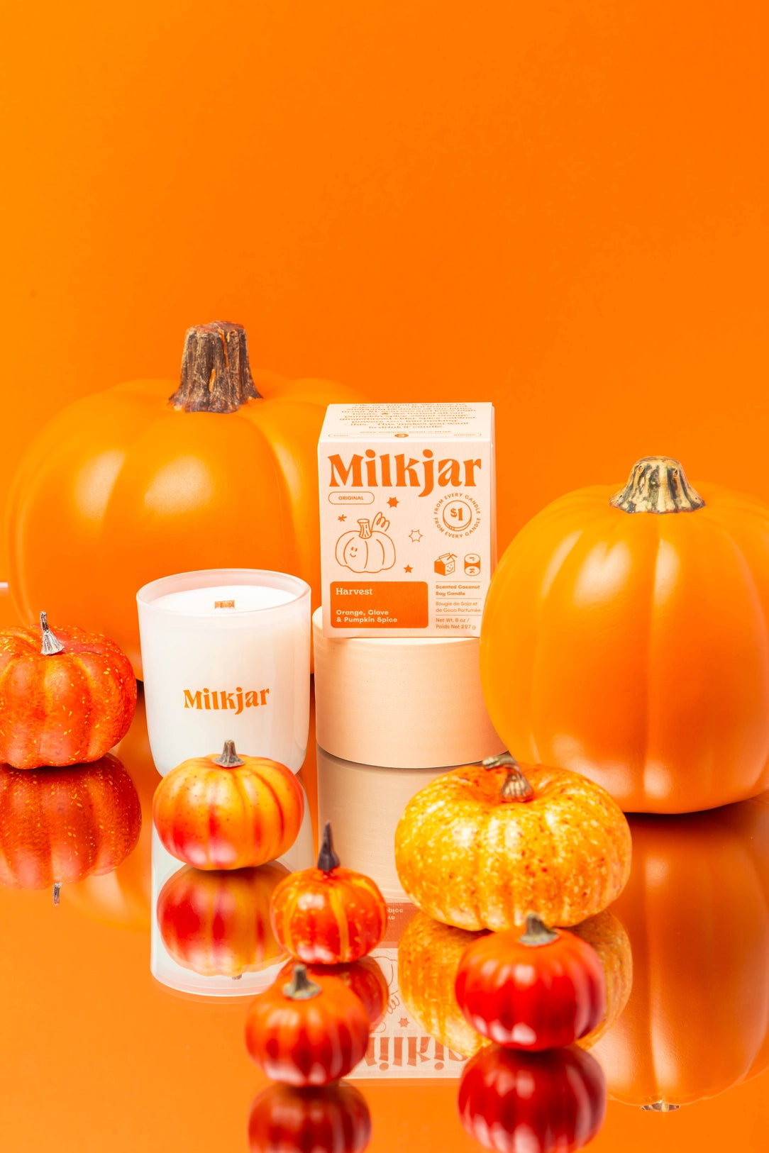 Bright Orange image showcasing an array of different pumpkins and branded 'harvest' milkjar candle co candle in the middle on a circular stand.