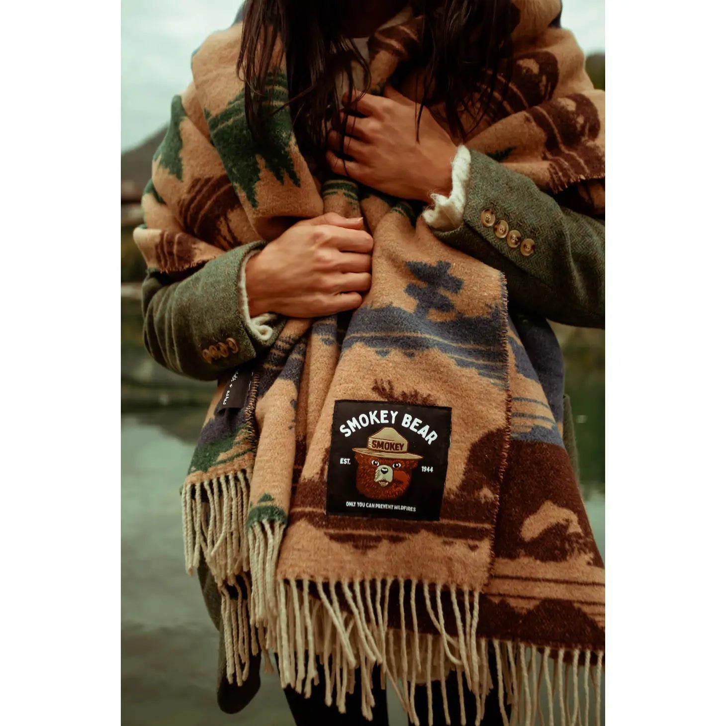 A Sackcloth & Ashes Smokey Bear Blanket - Smokey Dungaree, featuring woven rows with wilderness scenes of trees, mountains, bears, deer, and human figures in neutral tones.
