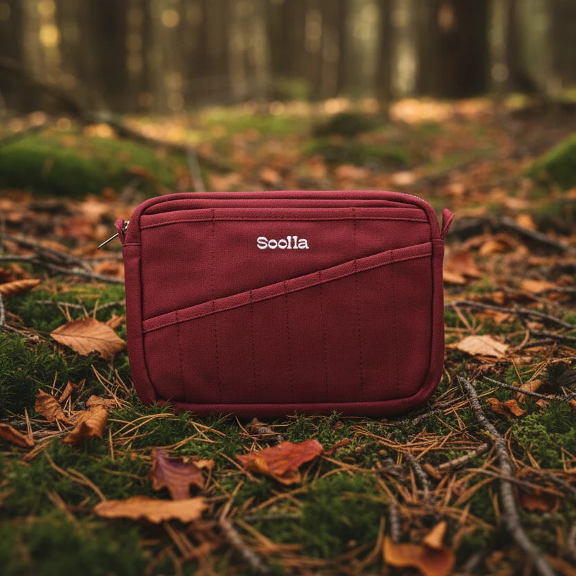 The Soolla® Studio Artist Stationery Pouch in Sangria on a mossy forest floor with autumn leaves and trees, perfect for artists.