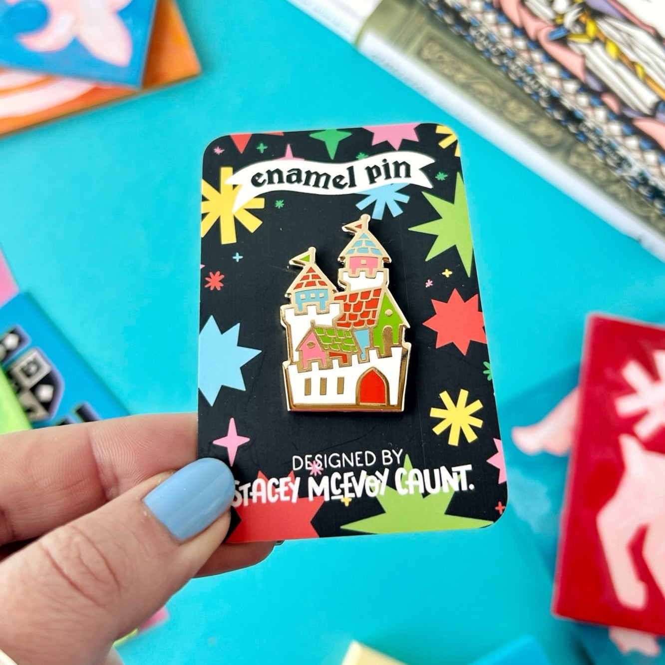 Hand displays Stacey McEvoy Caunt Medieval Castle Enamel Pin on branded backing card, collectible accessory gift idea.