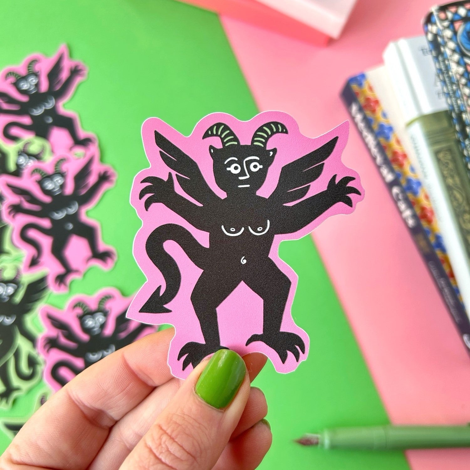 A hand with green nails displays the Stacey McEvoy Caunt Pink Devil Medieval Vinyl Sticker, vibrant and perfect for planners.