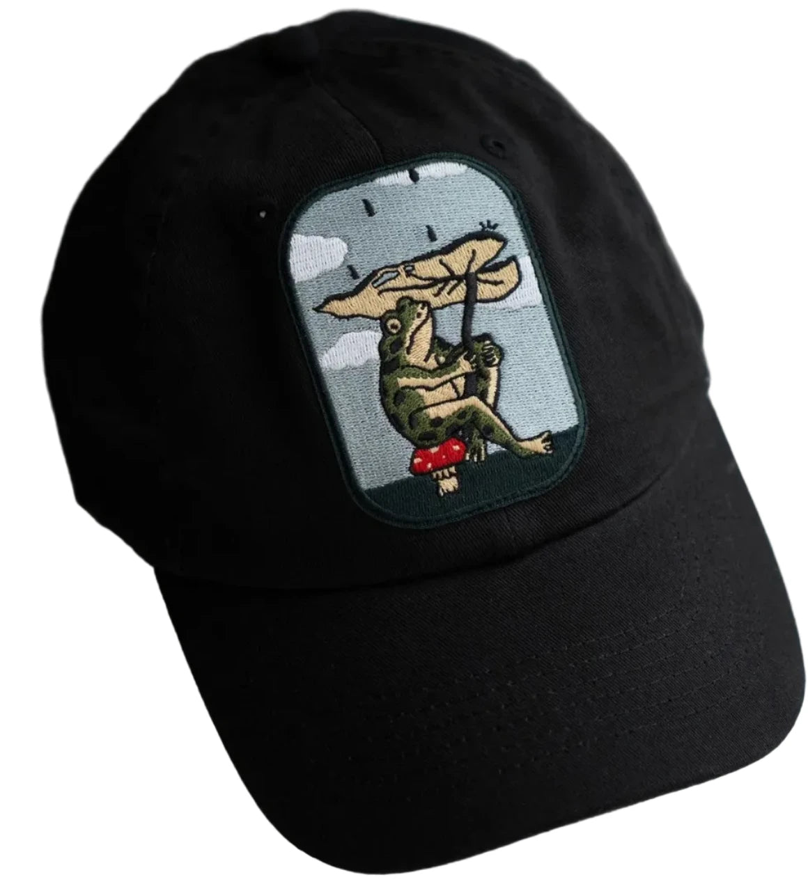 Trendy black dad hat with frog holding umbrella on red mushroom patch by Stay Home Club. Leaf Umbrella embroidered cap.