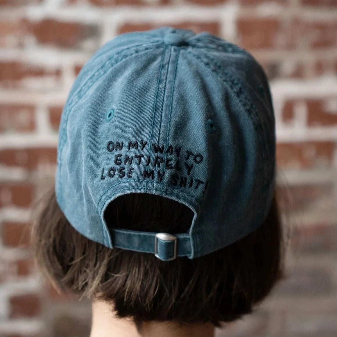 Vintage teal Stay Home Club Lose My Sh** Dad Cap on model standing by a brick wall, trendy streetwear hat fashion 2024.