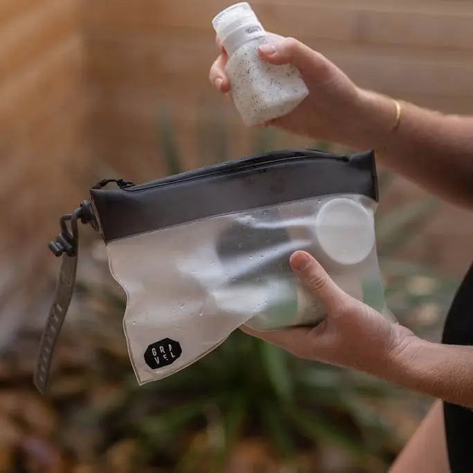 Person holding the Gravel Outdoor The Pouch, a 3-1-1 TSA-compliant travel shower bag, outdoors in bright natural light.
