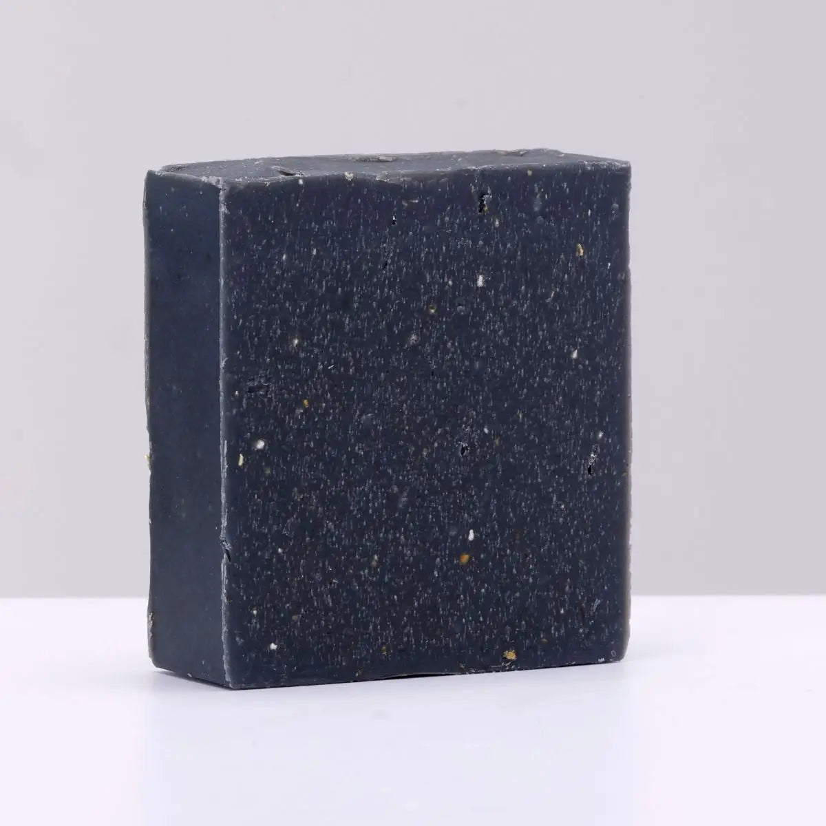 The Black Stuff Soap Atlantic Pine Tar bar with white specks on gray background, premium natural handmade soap for deep cleansing.