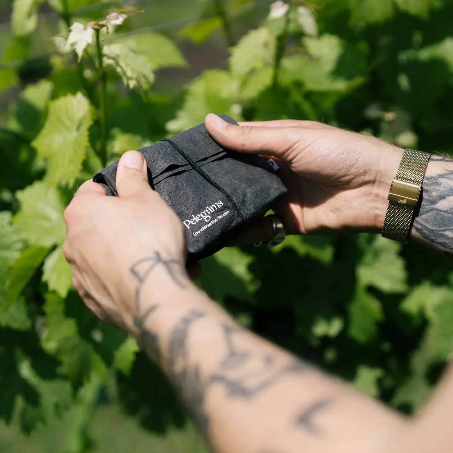 A black toiletry bag featuring Pelegrims branding, containing travel sizes of facial balm and hand pomade, along with a dropper bottle of facial oil infused with Pinot Noir Grape Extract, known as the Pelegrims Exploration Set.