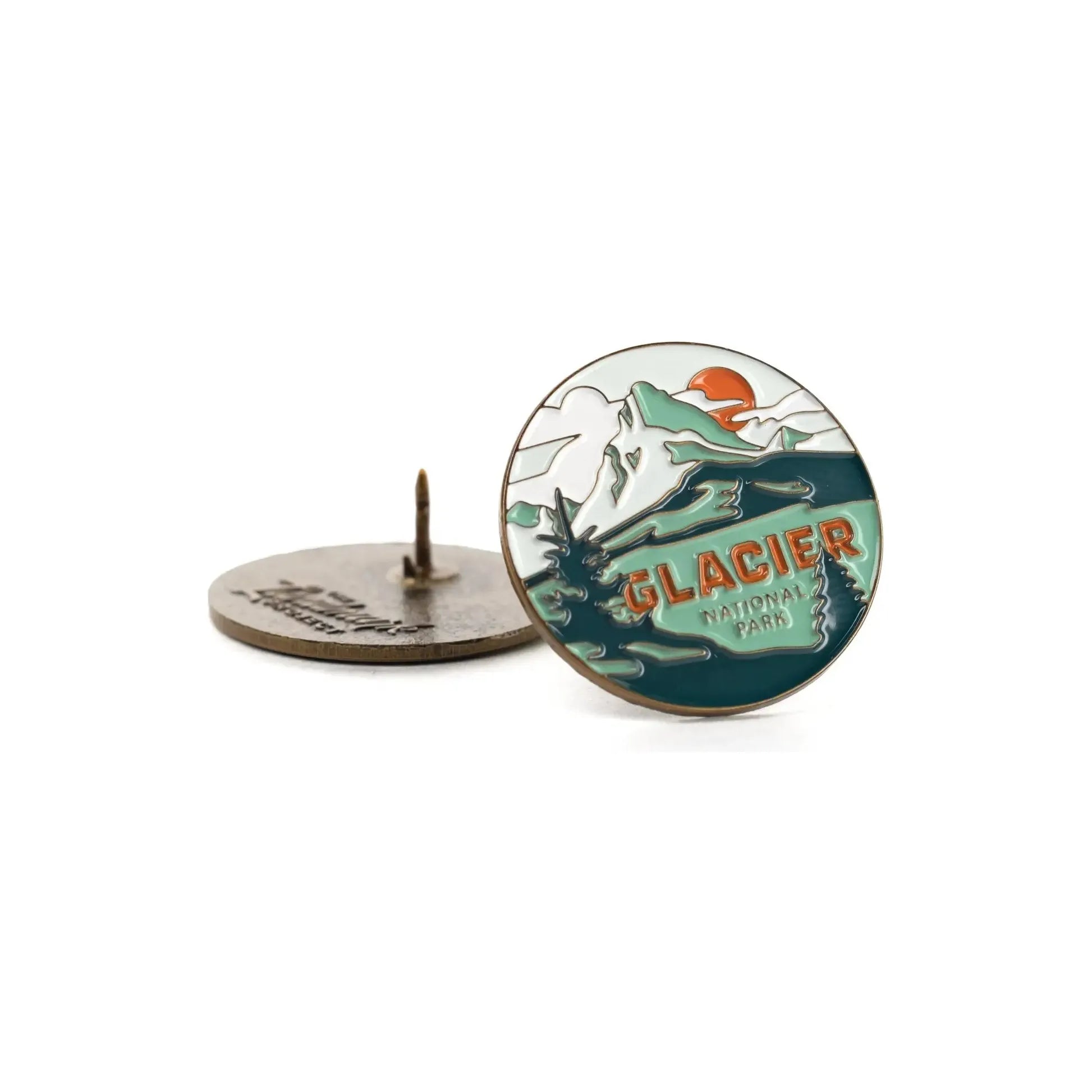 The Landmark Project Glacier National Park Pin showcases a beautifully designed mountain, sunset, and lake scene. The reverse side includes a secure clasp, and the pin is presented in sustainable packaging.