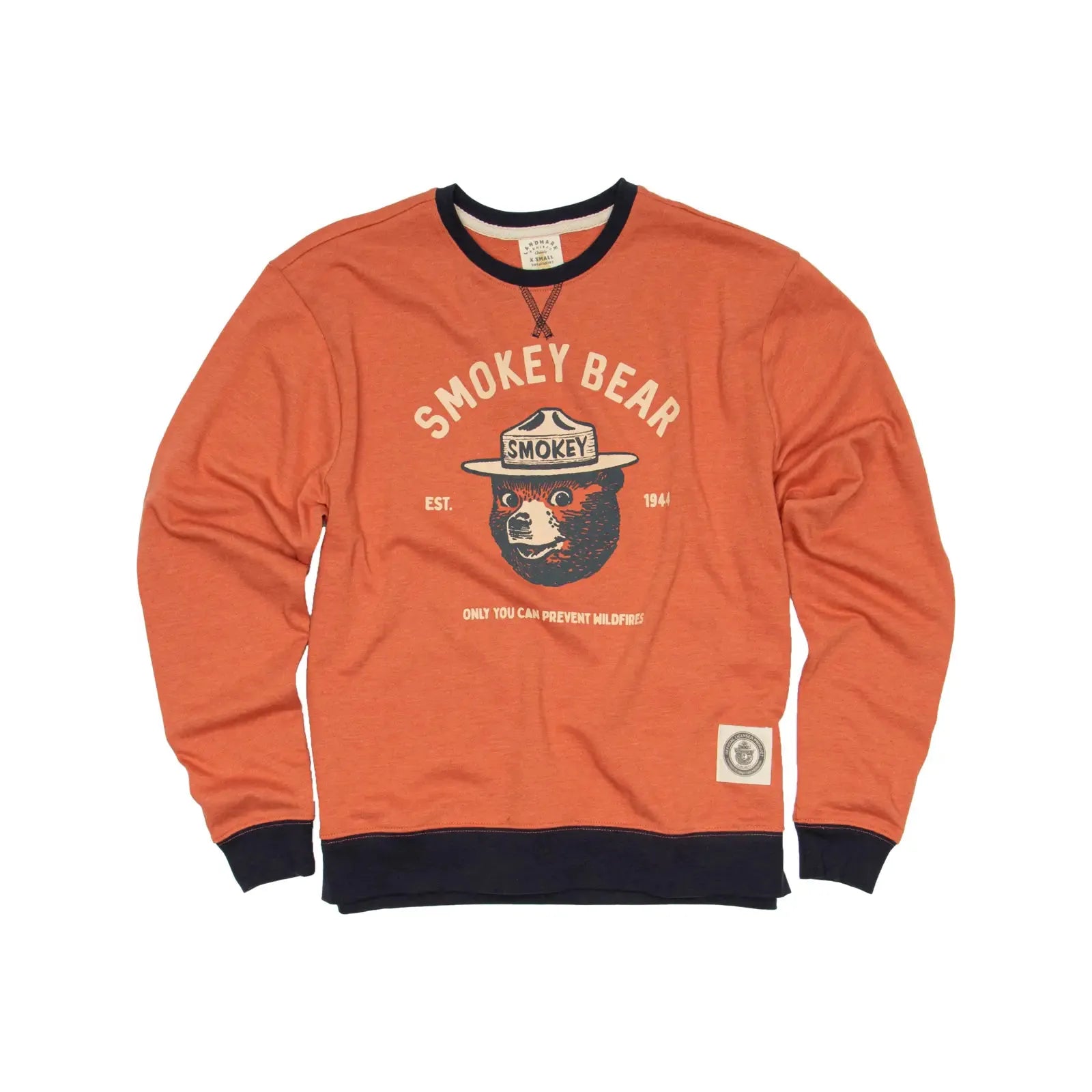 The Landmark Project Smokey Bear Heritage Varsity Orange Sweatshirt features a Smokey Bear graphic with text that reads "Smokey Bear Est. 1944" and "Only You Can Prevent Wildfires!" Made in Guatemala with recycled polyester, this sweatshirt has a black collar and cuffs.