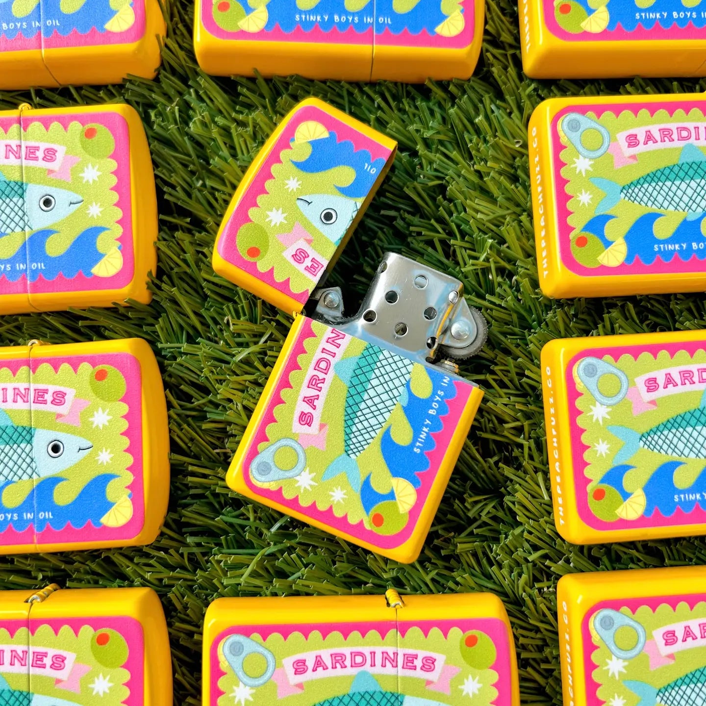 The Peach Fuzz Tinned Sardine Refillable Lighters displayed on grass, one open; unique eco lighter gift for outdoor lovers.