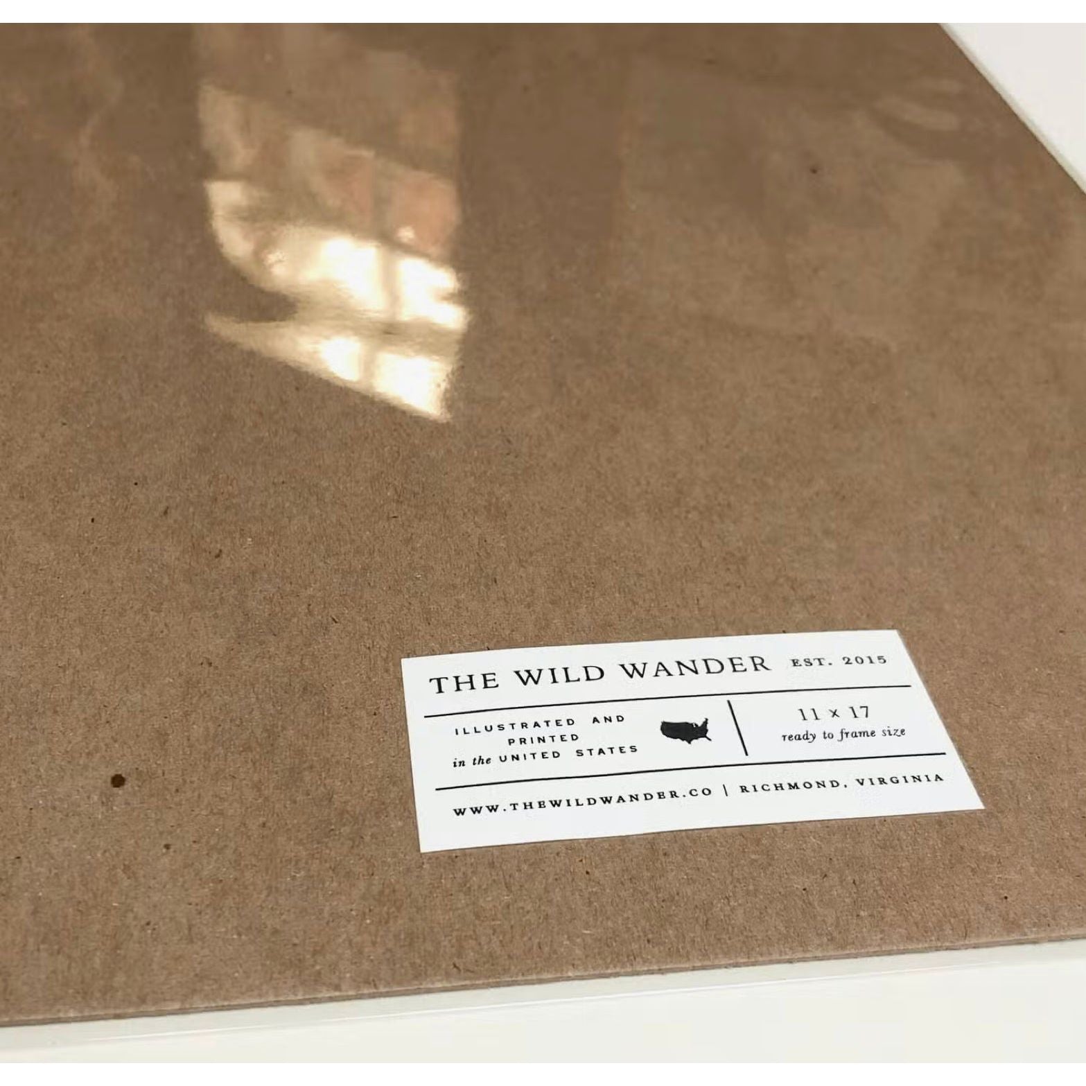 Close-up of a cardboard backing with a label reading "The Wild Wander Yellowstone Field Guide Print (11x17)," detailing brand and product dimensions, adorned with an exquisite letterpress chart capturing the flora and fauna of Yellowstone National Park.