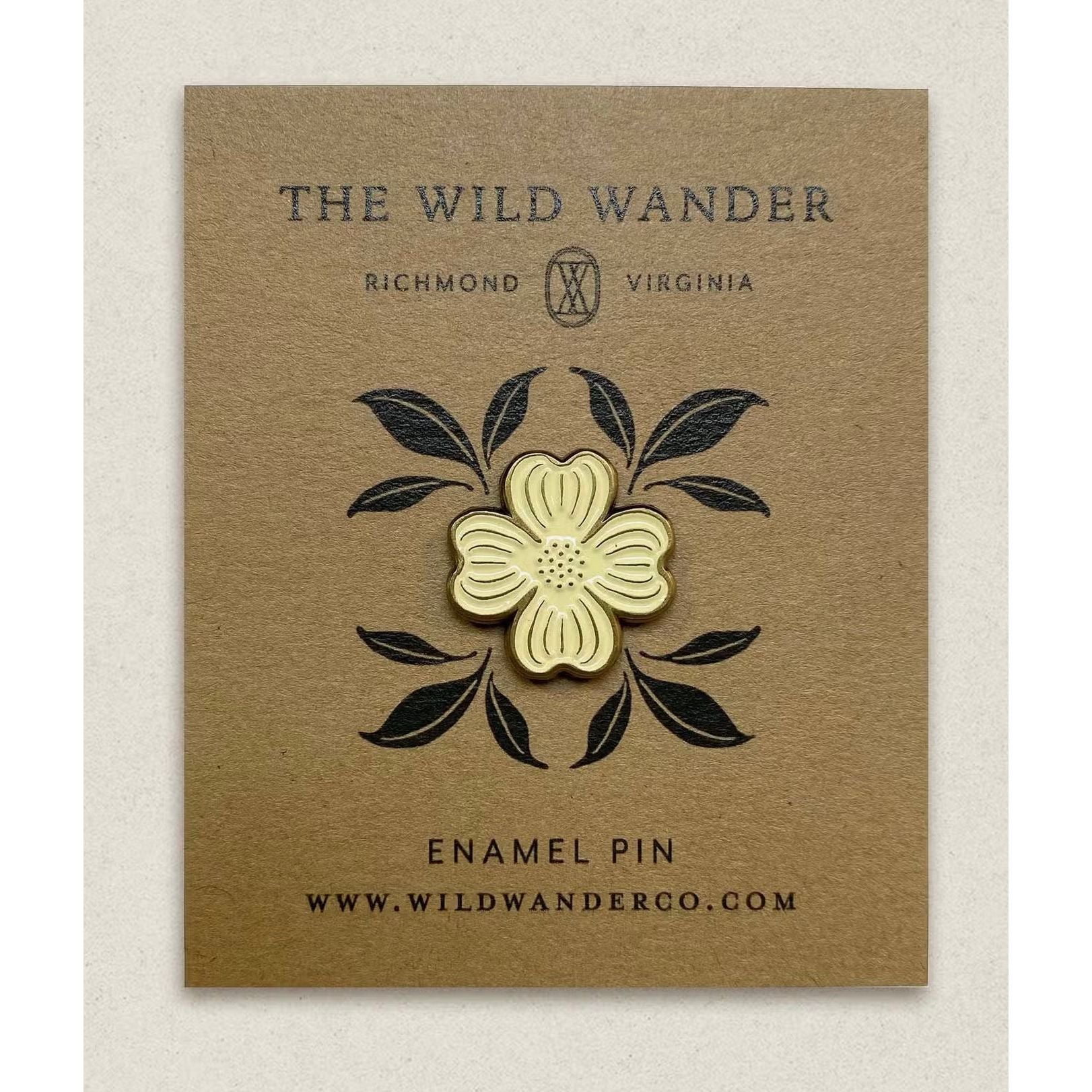 The Wild Wander Dogwood Lapel Pin is an ivory soft enamel pin featuring a flower design, presented on a brown card that displays the text "The Wild Wander," "Richmond, Virginia," and "www.wildwanderco.com." The pin includes elegant antique gold accents.
