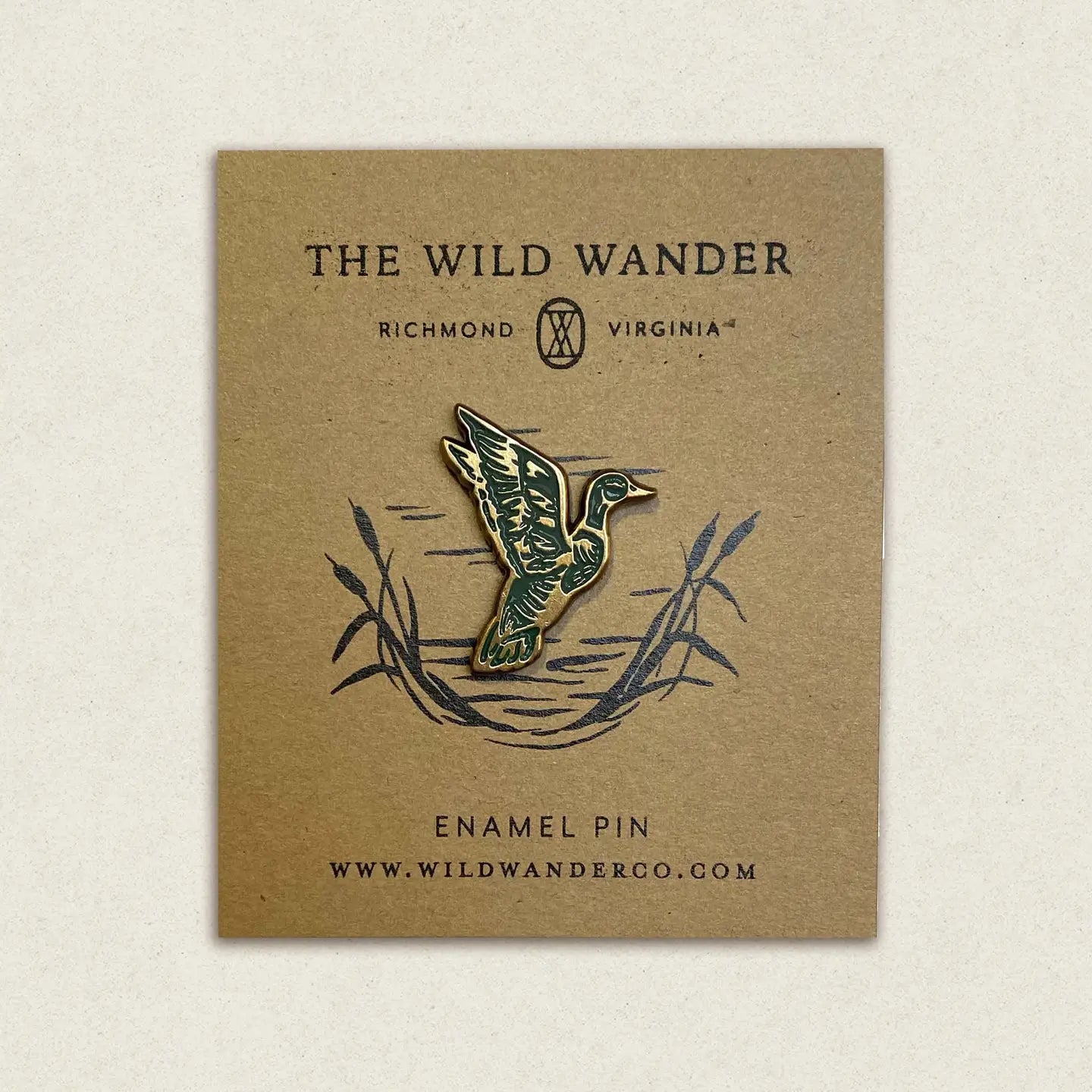 The Wild Wander Mallard Duck enamel pin in green and gold displayed on branded card with reeds, logo, and website info.