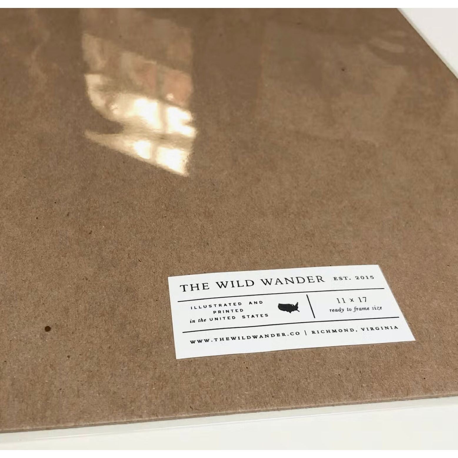 Close-up of a brown cardboard packaging with a sticker that reads, "The Wild Wander, Est. 2015, Richmond, Virginia," featuring an 11x17 hand-illustrated letterpress chart of Texas flora and fauna titled "The Wild Wander Texas Field Guide Print.