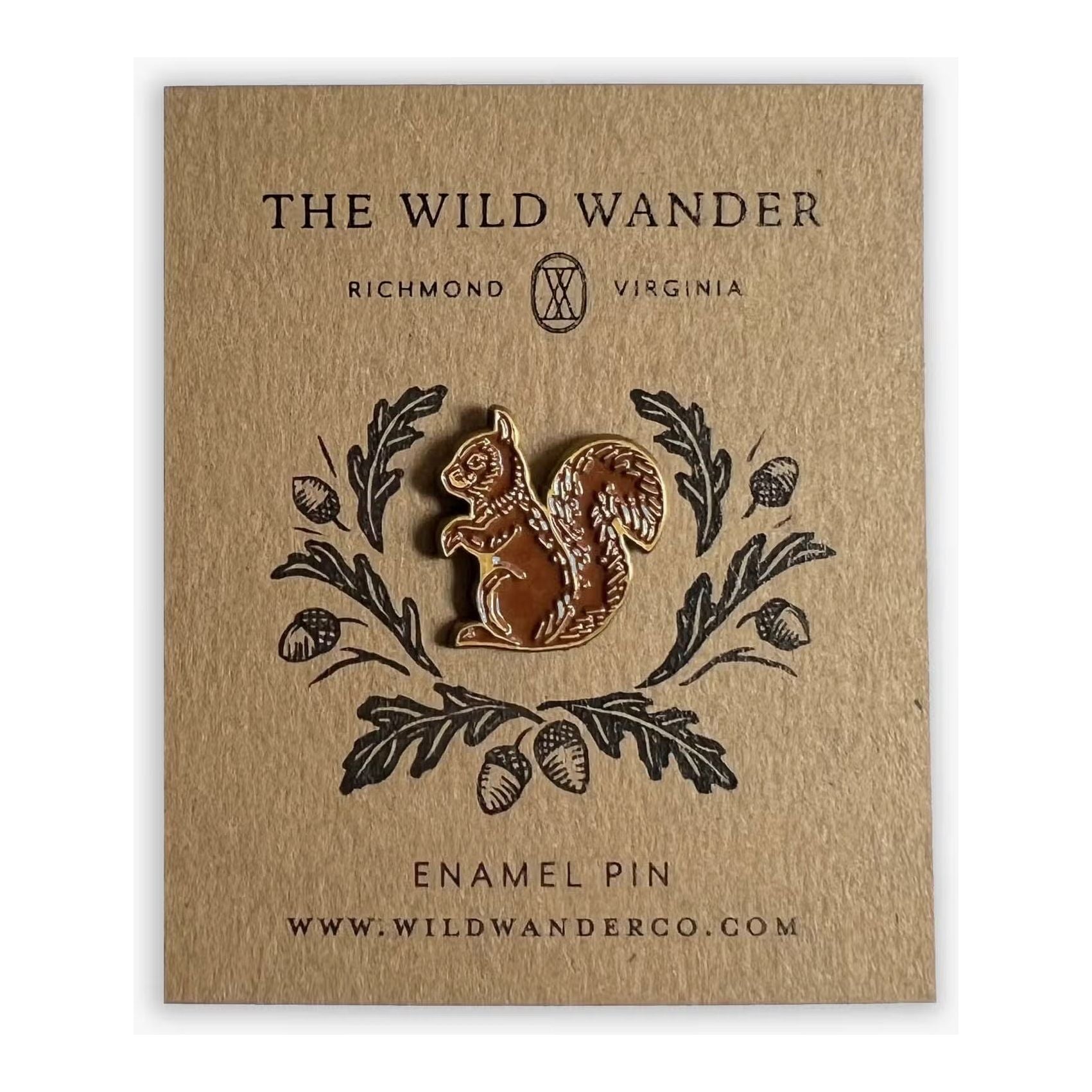 A custom illustrated enamel lapel pin with an antique gold finish featuring a golden squirrel, presented on a brown card adorned with oak leaves, acorns, and "The Wild Wander" branding along with the website www.wildwanderco.com.