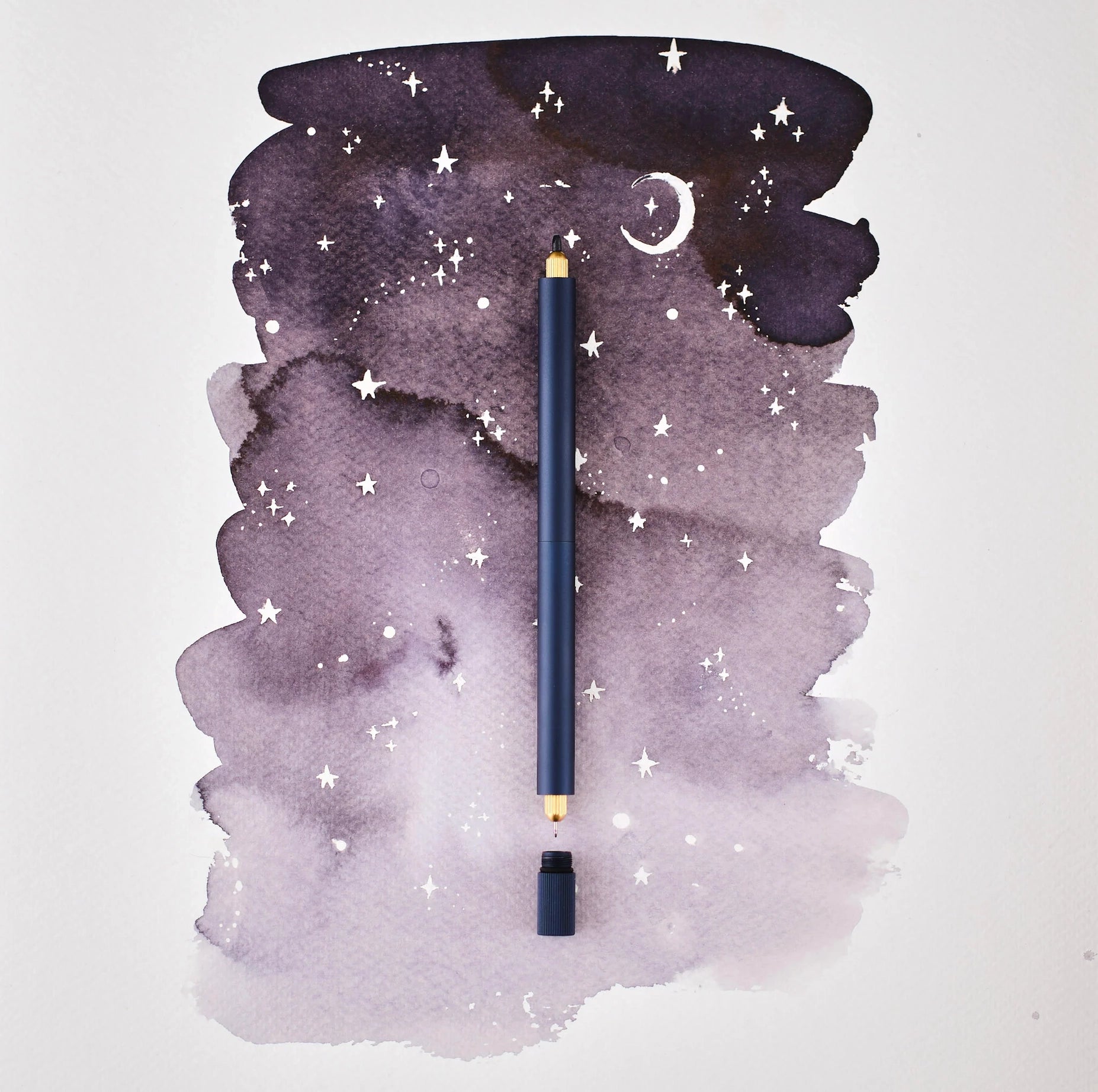 The Tom’s Studio Lumos Pro Duo Midnight Pen upright on a purple starry background with a crescent moon, luxury writing pen.