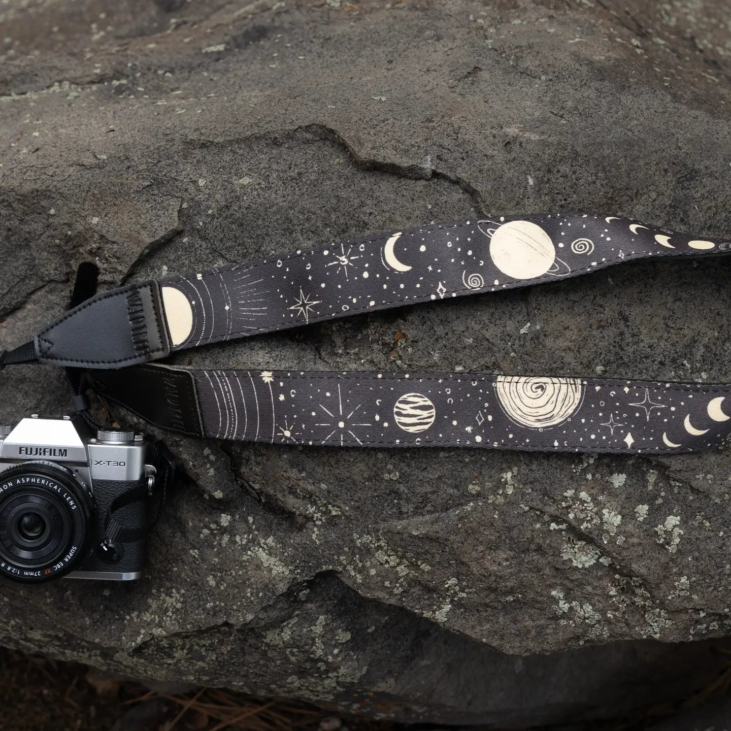 Fujifilm camera with stylish Wildtree Sun & Moon Camera Strap placed on large gray rock, perfect outdoor photography gear setup.