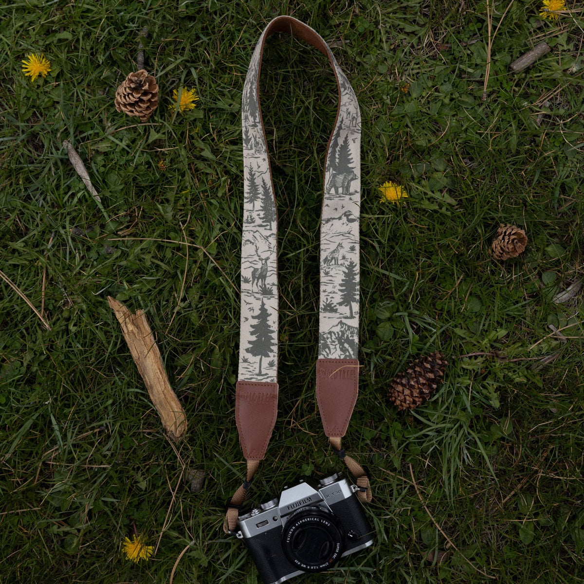 Forager Provisions LTD Wildtree camera strap with woodland mountain print attached to a Fujifilm camera on grass.