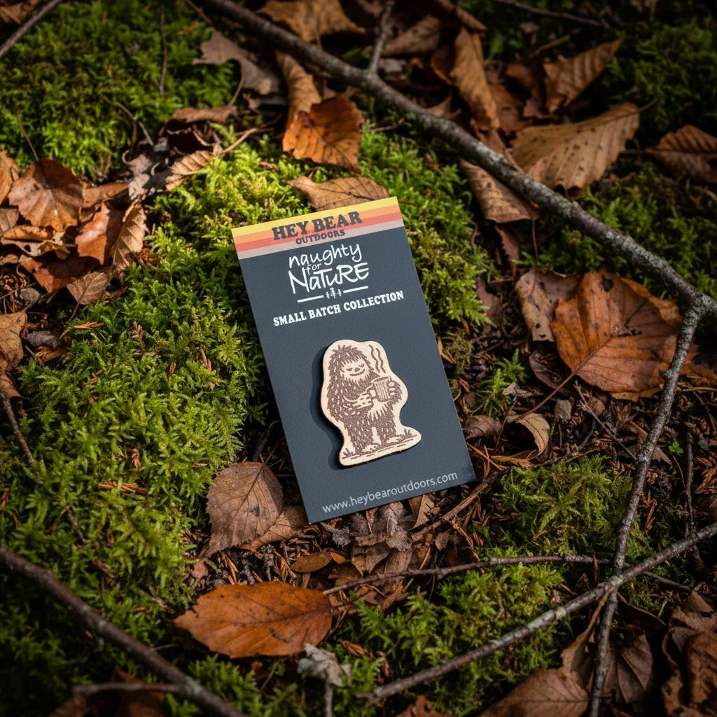 Forager Provisions LTD Hey Bear Outdoors Bigfoot wooden pin badge on a branded backing card resting on forest moss.