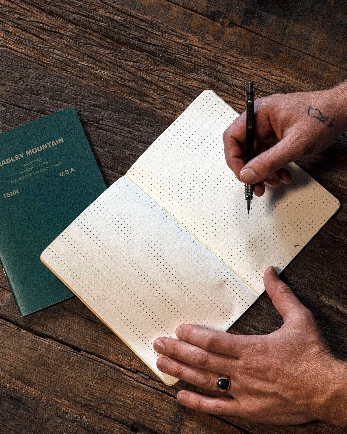Forager Provisions LTD Bradley Mountain dot grid journal open on a rustic wooden desk with a hand writing in it
