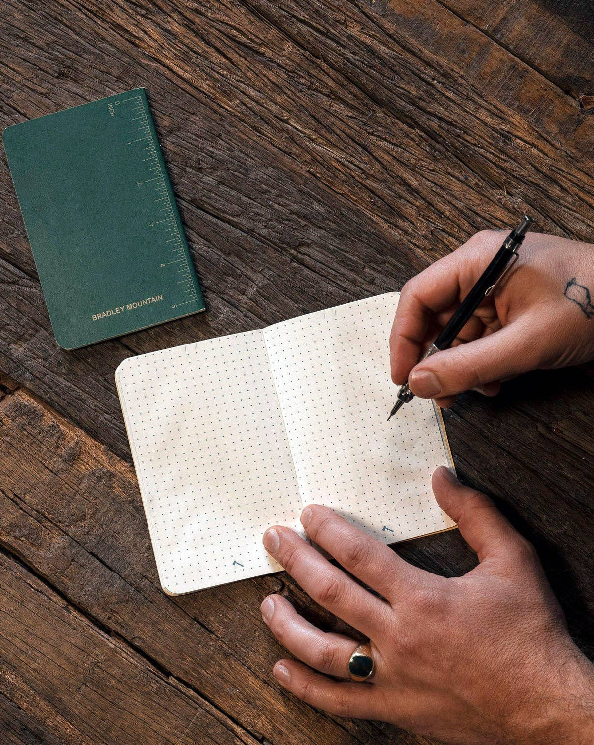 Forager Provisions LTD Bradley Mountain pocket journals with dot grid pages being used for writing on a wooden table.
