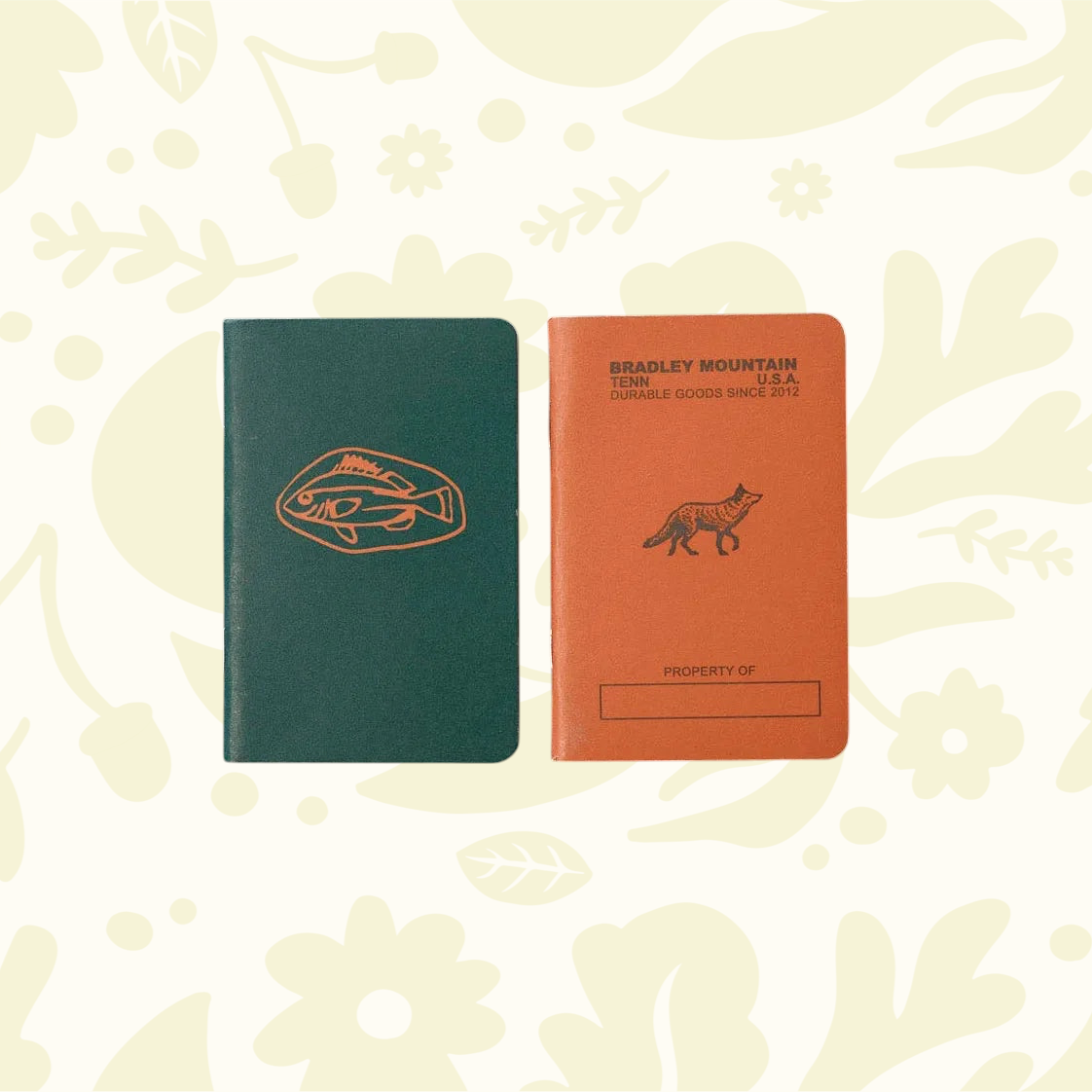 Forager Provisions LTD Bradley Mountain pocket journals in green and orange with fish and fox illustrations on wood.