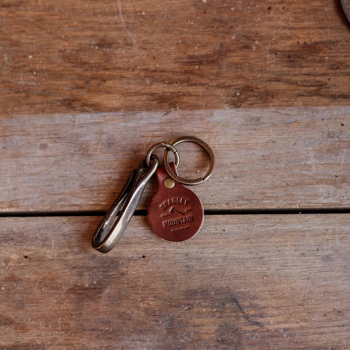 Forager Provisions LTD Bradley Mountain brass fish hook key fob with a branded leather tag on a rustic wooden surface.