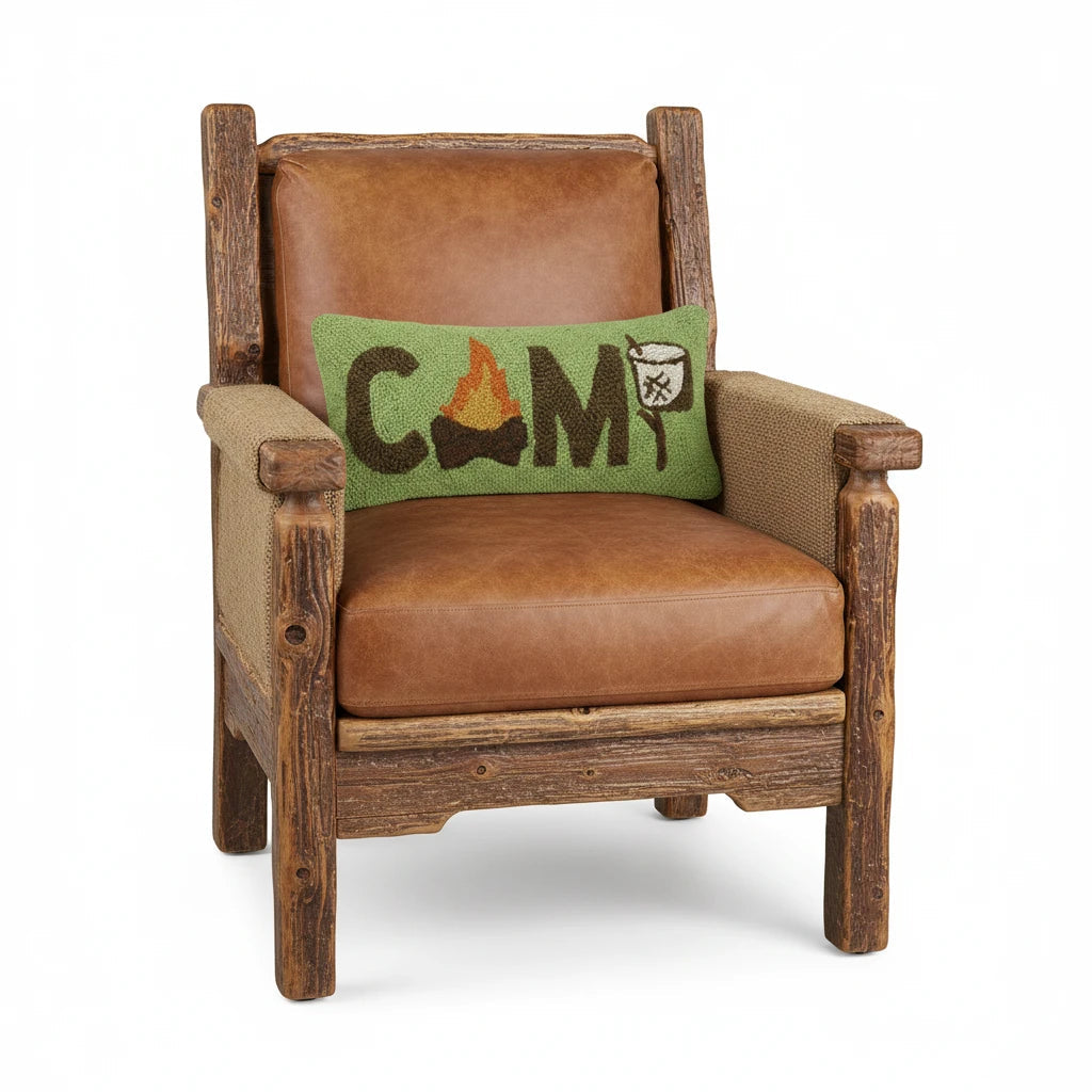 Rustic wood armchair with brown leather cushions, featuring CAMP Marshmallow wool hook cushion with campfire graphic.