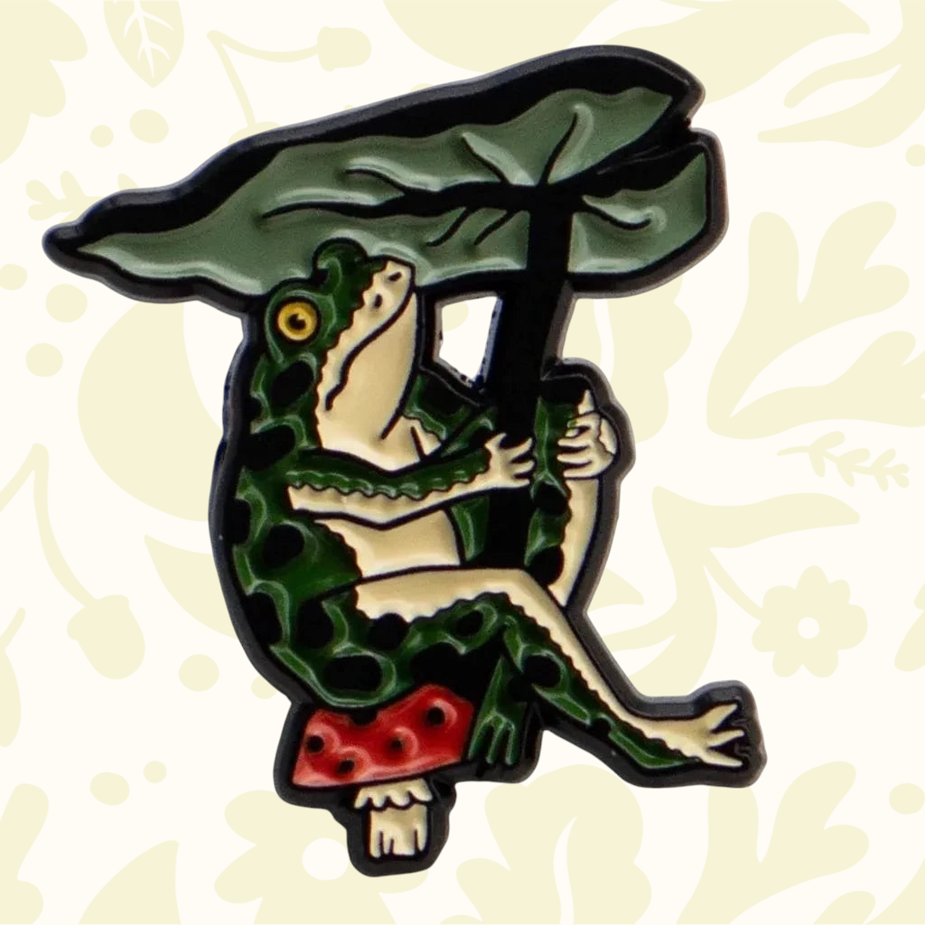 Forager Provisions LTD enamel pin featuring a green frog sitting on a mushroom under a large leaf umbrella