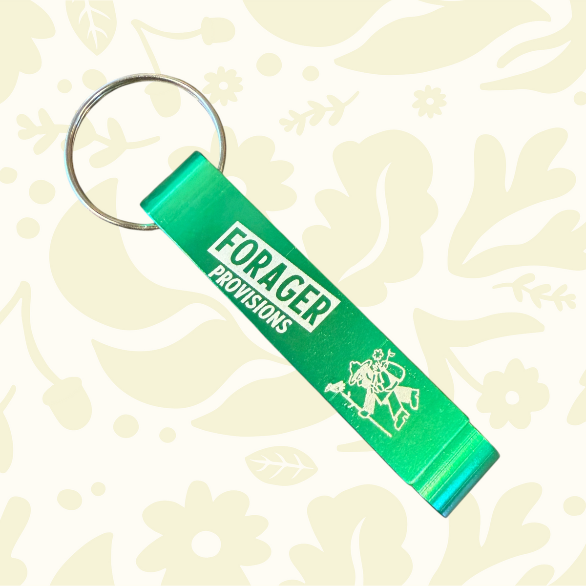 Forager Provisions LTD metallic green bottle opener keyring with white logo and graphic on a textured surface