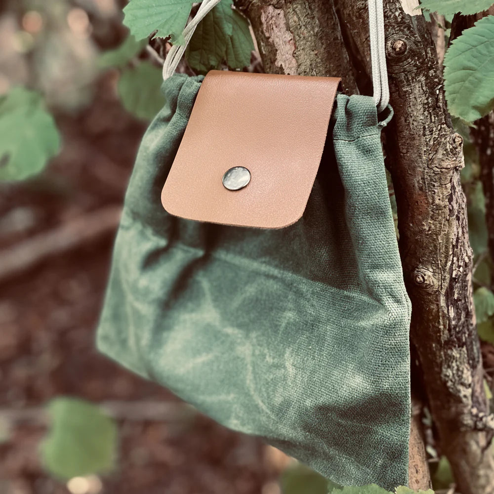 Forager Provisions LTD green canvas forage bag with vegan faux leather flap and popper closure hanging on a tree branch.