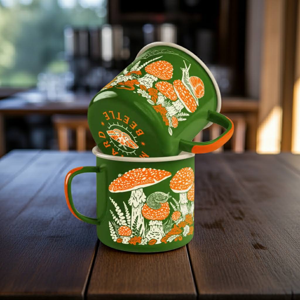 Stacked green enamel mugs with mustard beetle, toad, and mushrooms designs on dark wood table in gentle natural light.