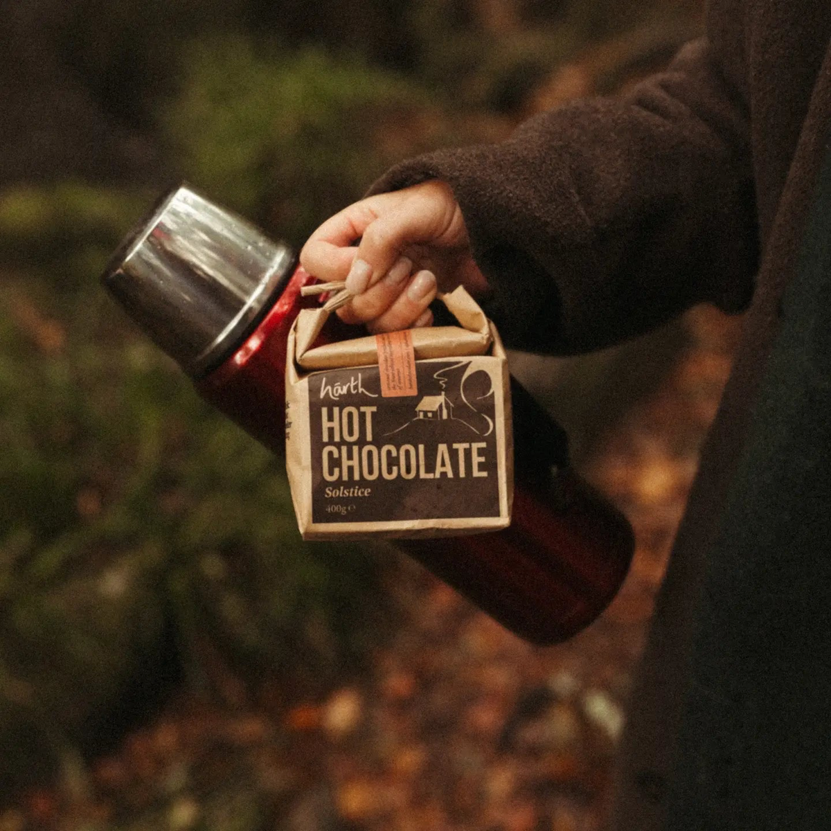 Forager Provisions LTD Harth Winter Solstice vegan spiced hot chocolate pouch held outdoors with a red thermos
