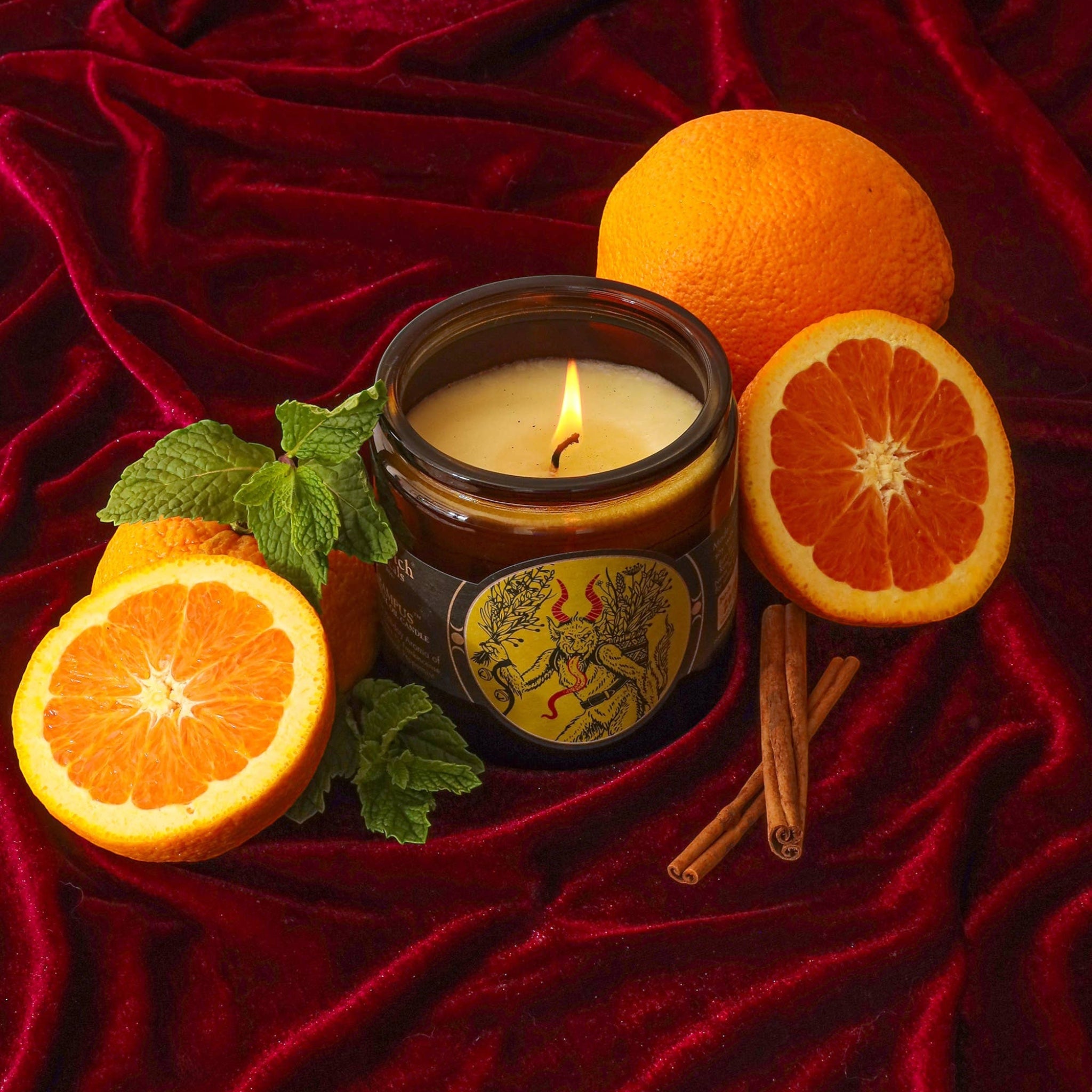 Forager Provisions LTD Sea Witch Botanicals Krampus soy wax candle in a glass jar on red velvet with oranges and mint.