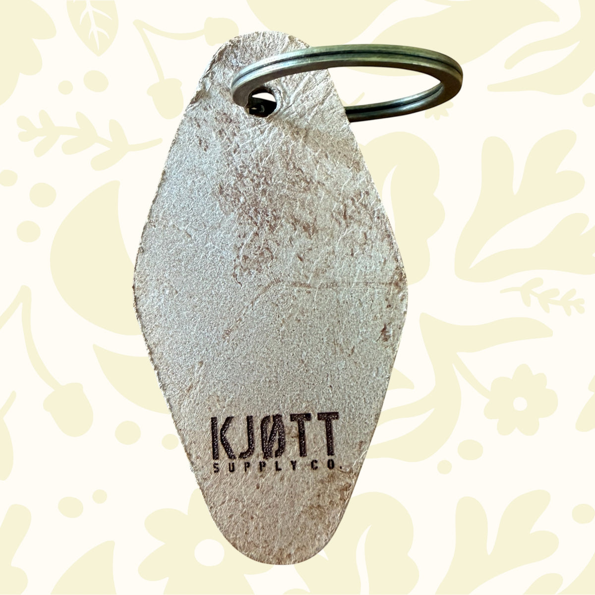Forager Provisions LTD Kjøtt Supply Co tan leather motel-style keyring with a brass ring on a wooden surface.