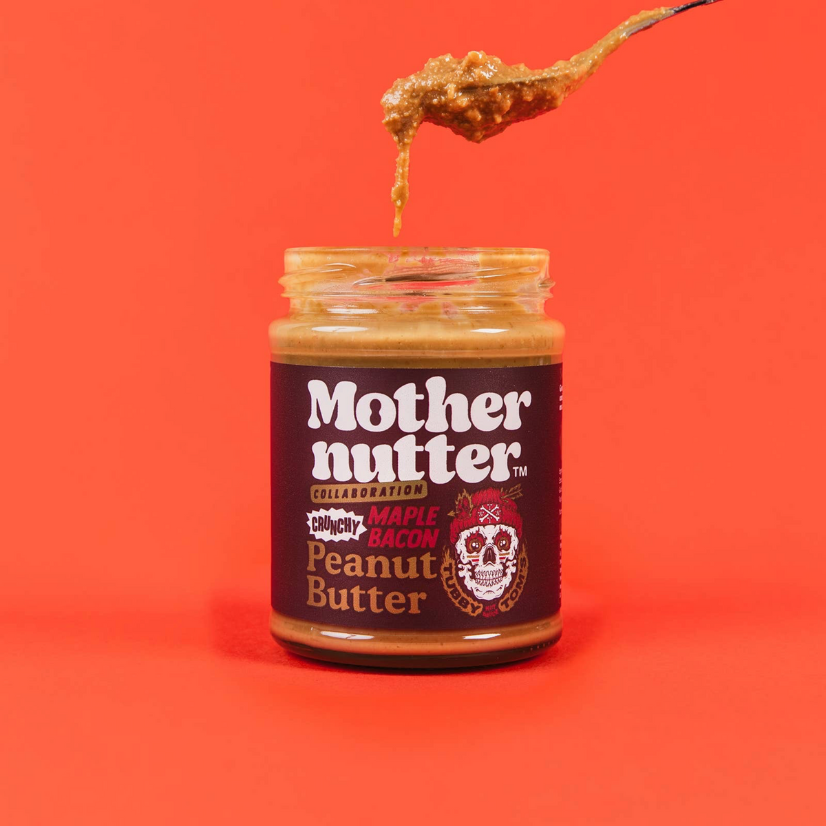 Forager Provisions LTD Mothernutter crunchy maple bacon peanut butter in a glass jar with a spoon dripping the spread.