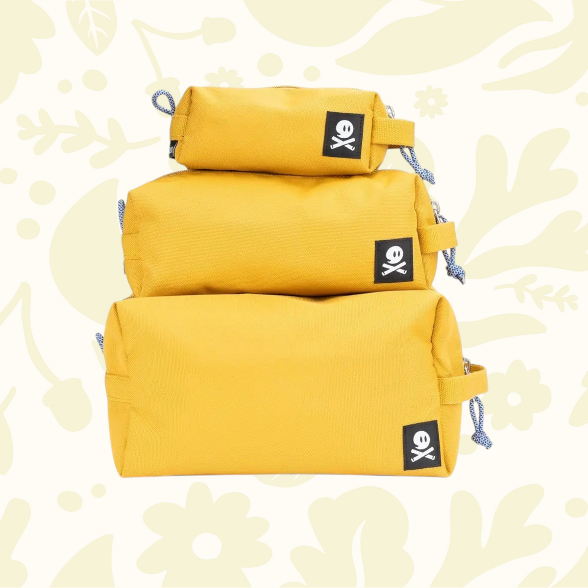 Three Ghost Outdoors ochre yellow Dopp Kits stacked on vibrant floral background, stylish travel toiletry bags display.